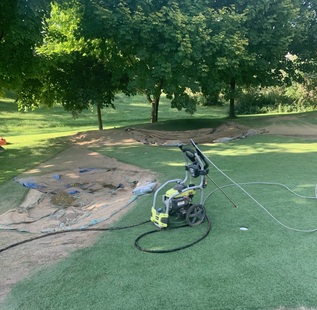 Golf green with artificial turf and power washer to clean the turf surrounding mature trees