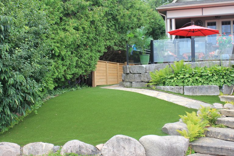 Artificial grass backyard installation with garden stones, fencing and outdoor patio area